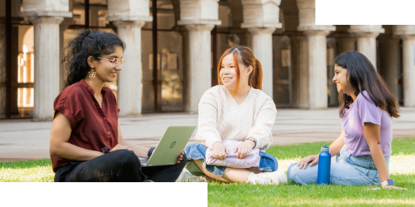 Three female students sitting on the lawn outside Winthrop Hall