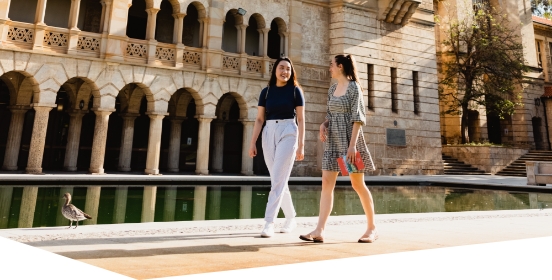 Two students walking in front of reflection pond near Winthrop Hall building 