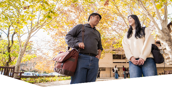 Two students standing outside the UWA Law building amongst the trees